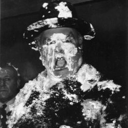 A man’s face is covered in cream as a result of a pie fight in the